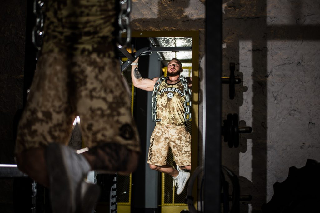 Sportowiec podciąga się na drążku w termoaktywnym ubraniu wojskowym